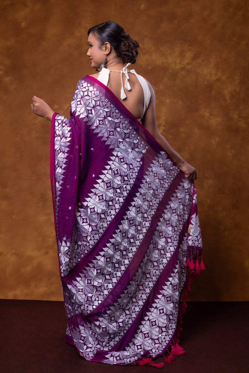 Woman wearing a purple and white patterned saree against a brown background