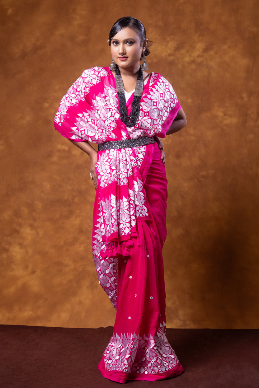 Woman wearing a pink saree with white patterns against a brown background