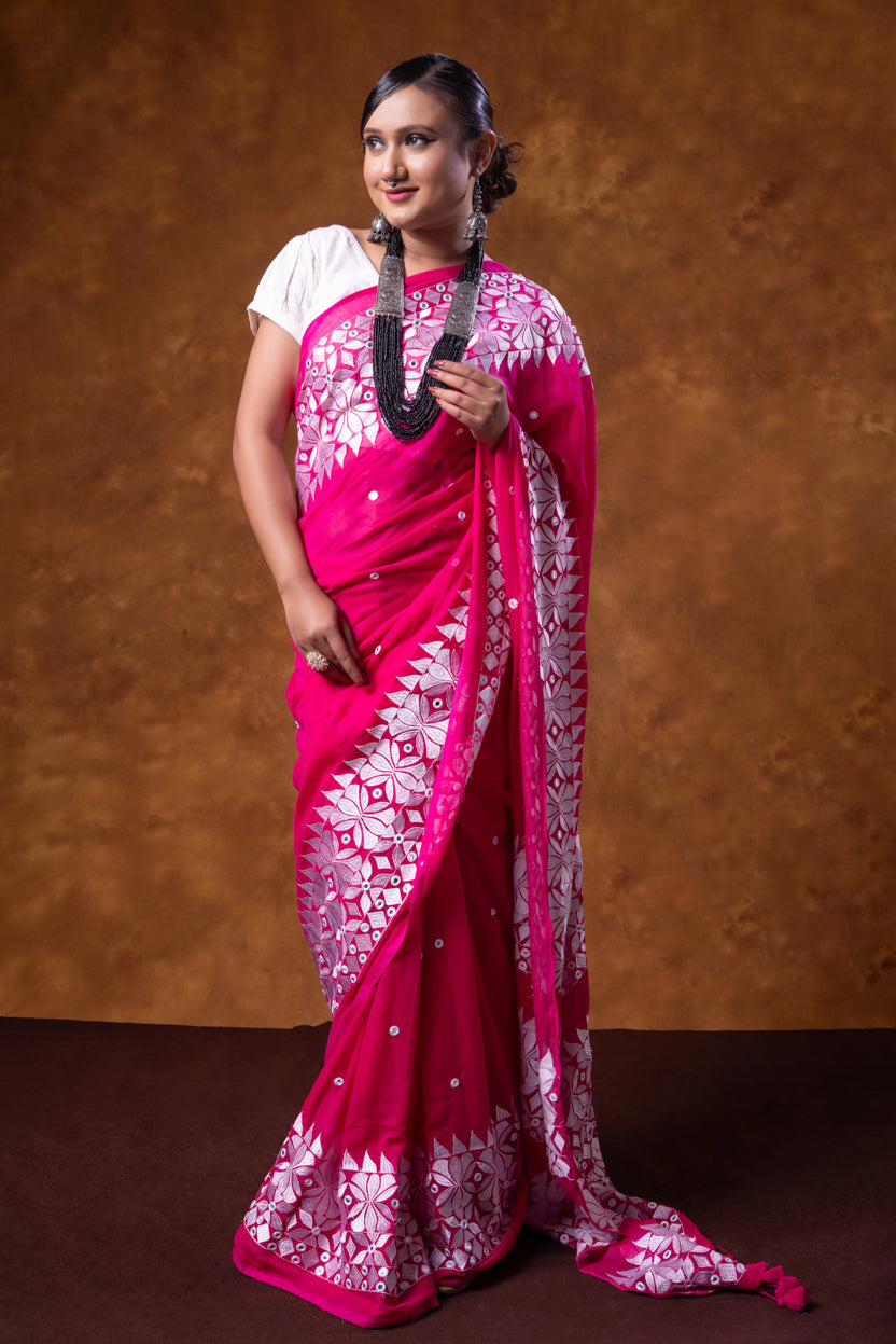 Woman wearing a bright pink saree with white patterns against a brown background