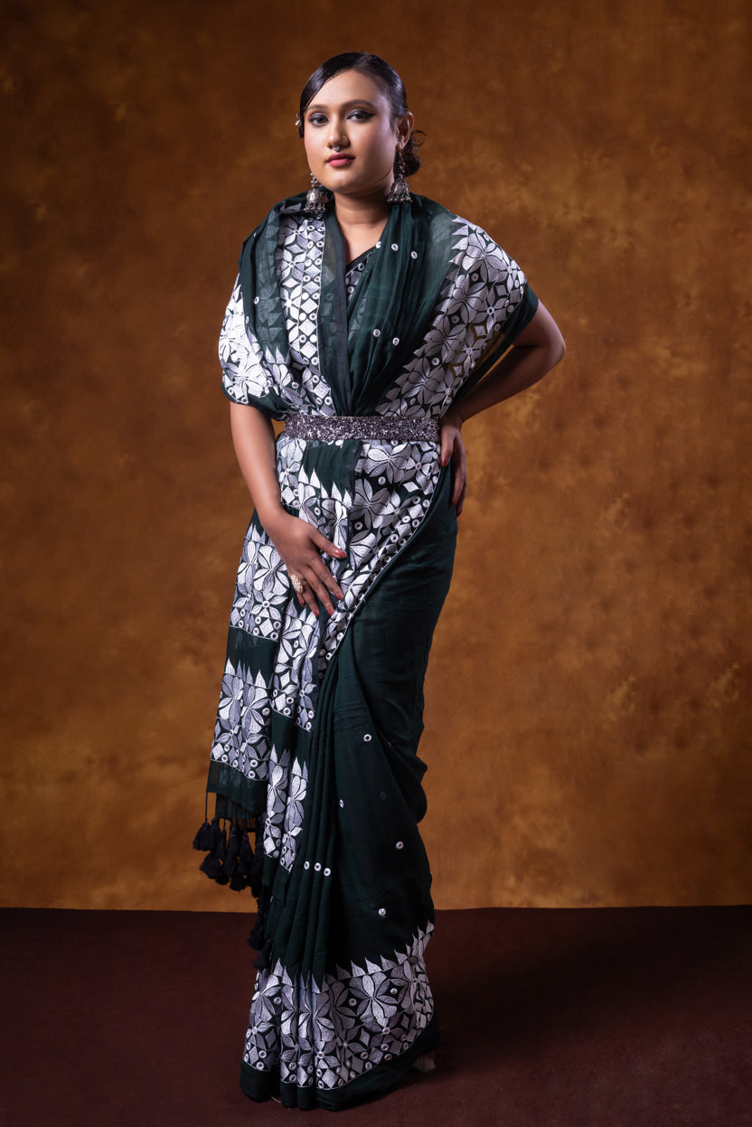 Woman wearing a black and white patterned saree against a brown background