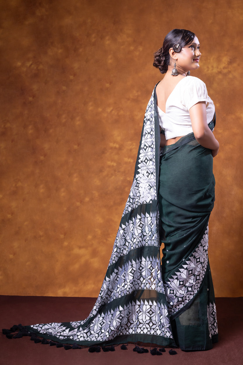 Woman wearing a green saree with a white and black pattern against a brown background