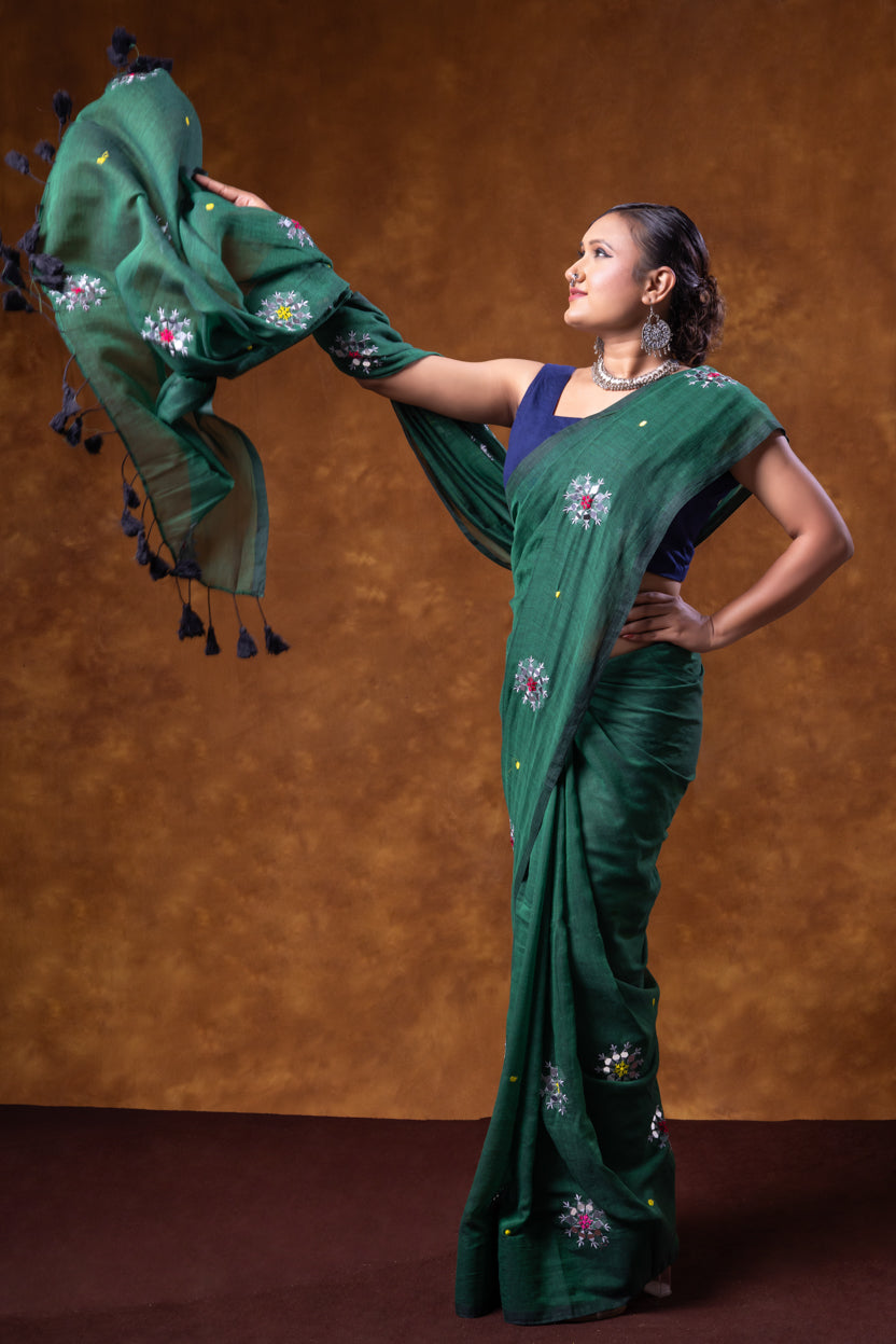 Woman in a green saree with floral patterns against a brown background