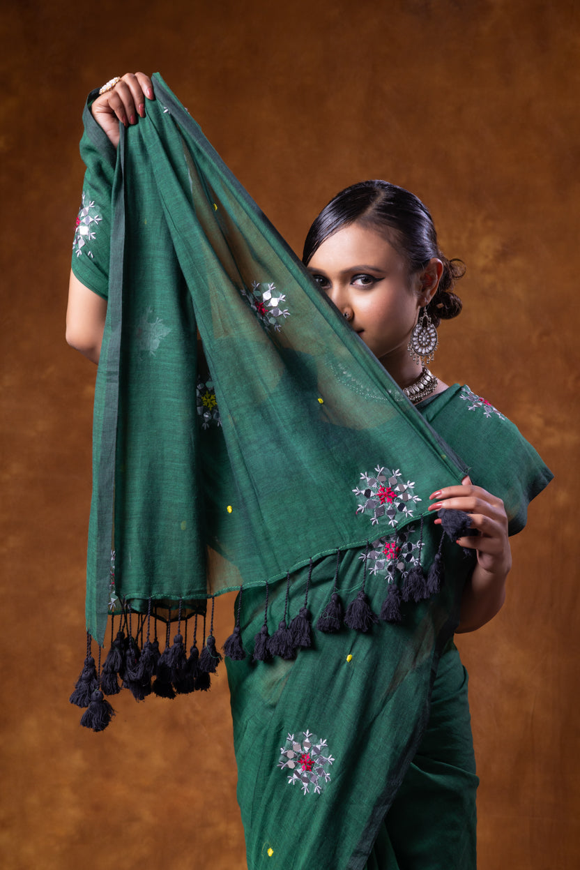 Woman holding a green saree with floral patterns against a brown background