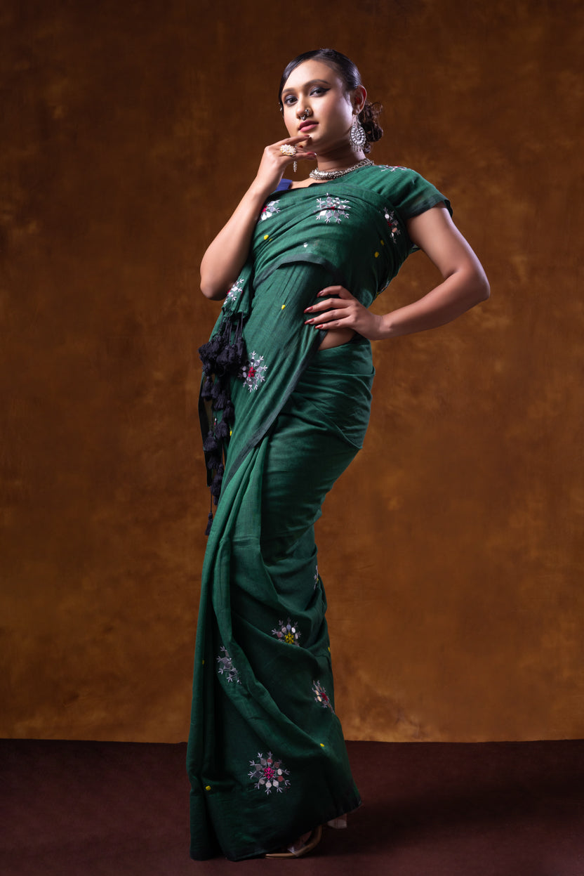 Woman wearing a green saree with floral patterns against a brown background