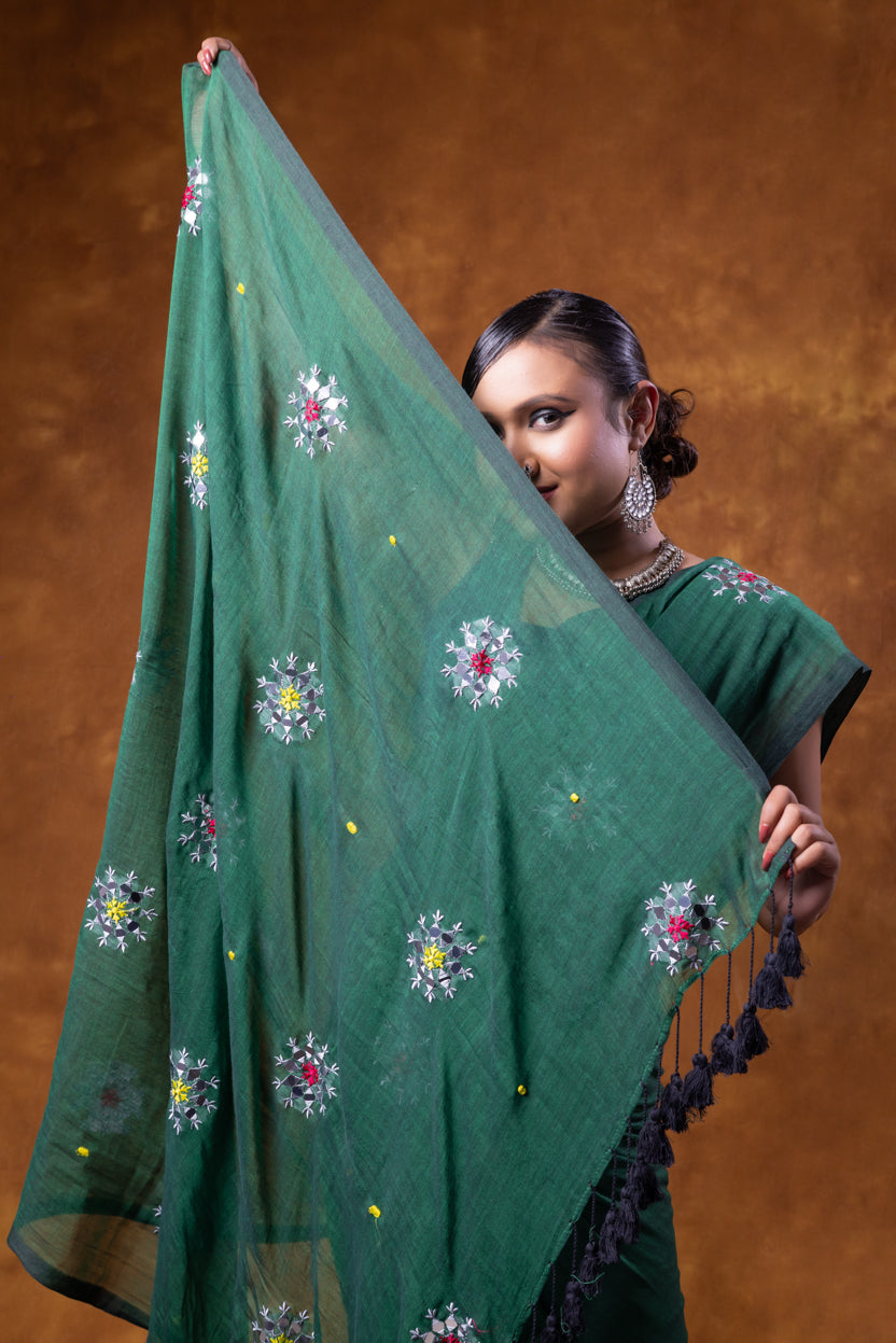 Woman holding a green embroidered saree against a brown background