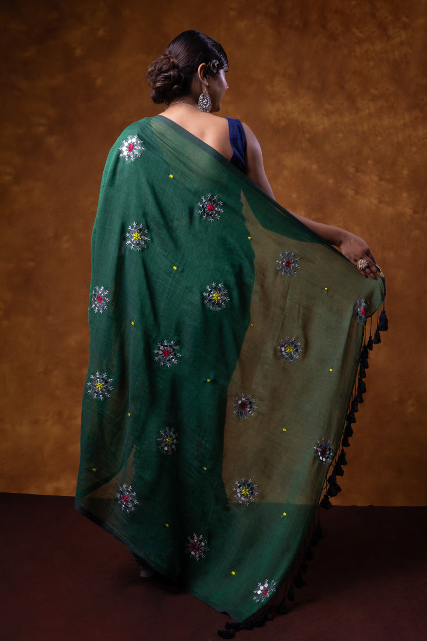 Woman wearing a green saree with floral patterns against a brown background