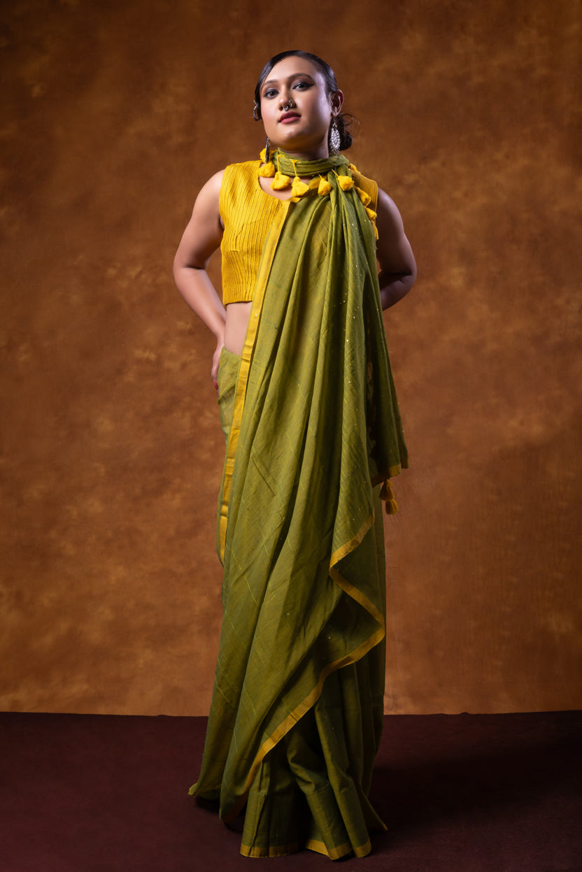 Woman wearing a yellow blouse and green saree against a brown background