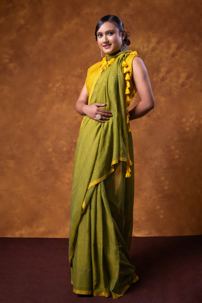 Woman wearing a green saree with yellow blouse against a brown background