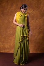 Woman wearing a green saree with a yellow blouse against a brown background