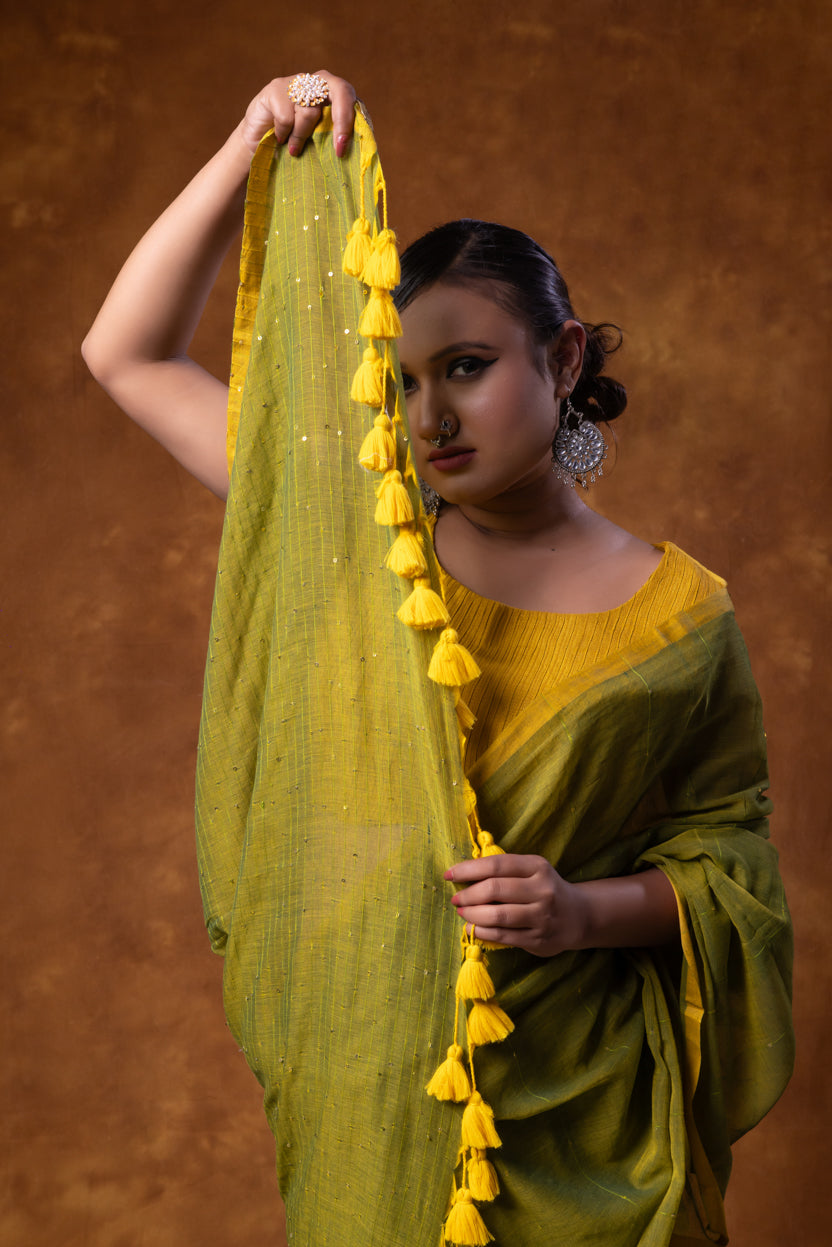 Woman holding a green saree with yellow tassels against a brown background