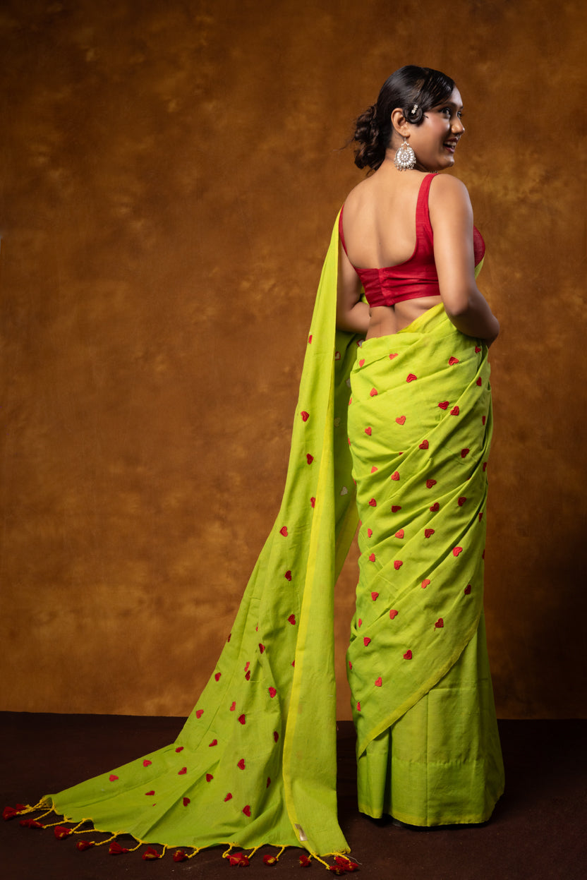 Woman wearing a bright green saree with red patterns and a red blouse against a brown background