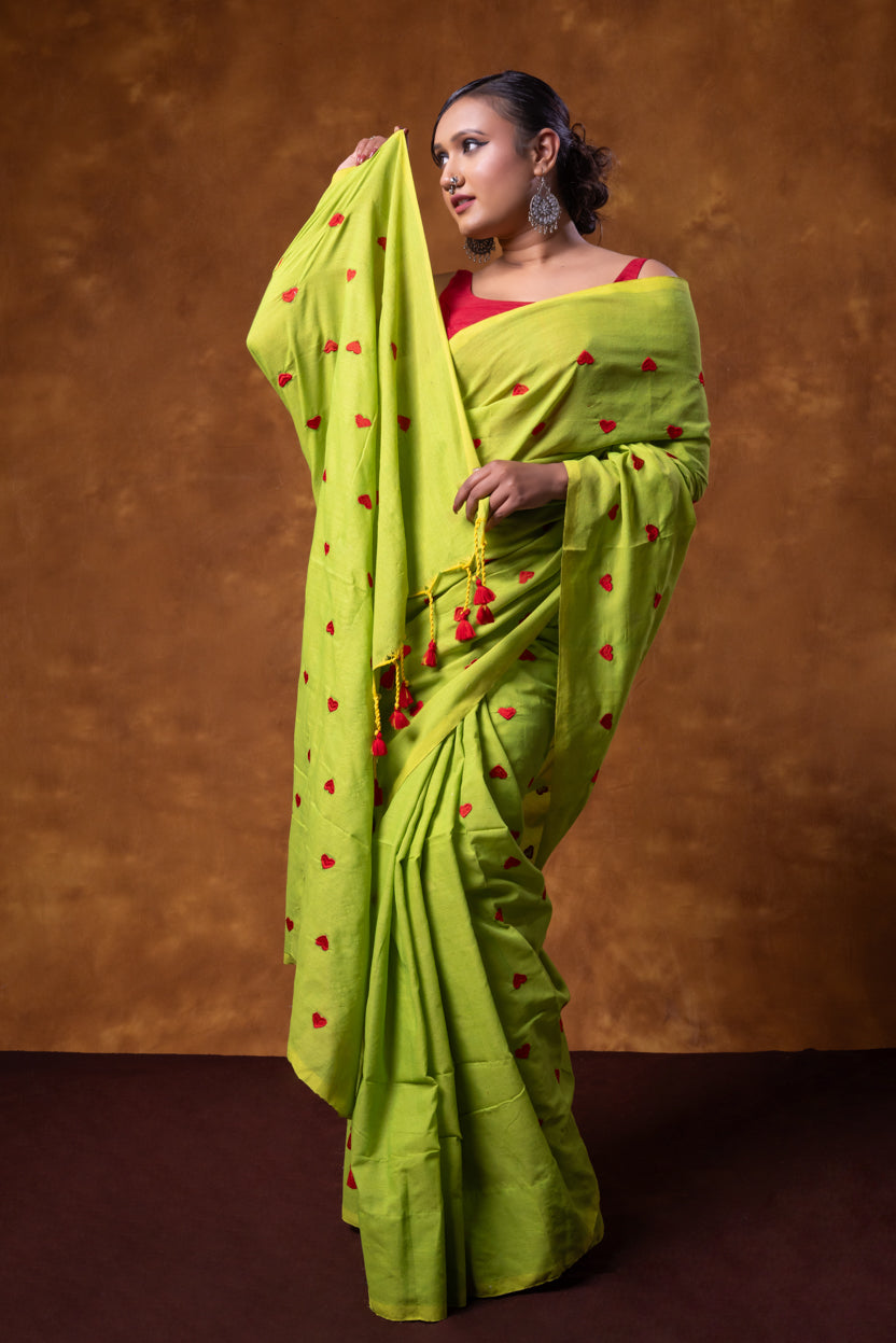 Woman wearing a bright green saree with red patterns against a brown background