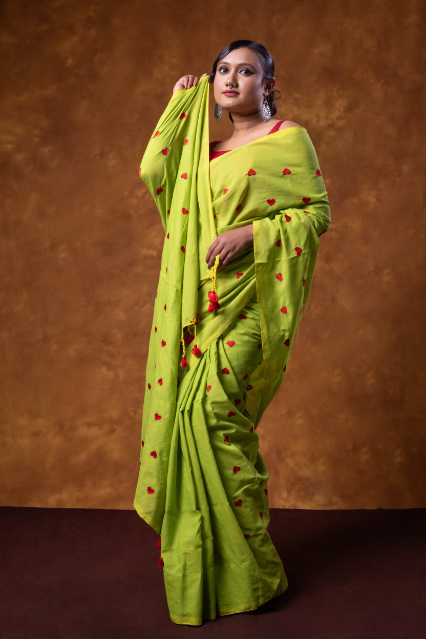 Woman wearing a bright green saree with red patterns against a brown background