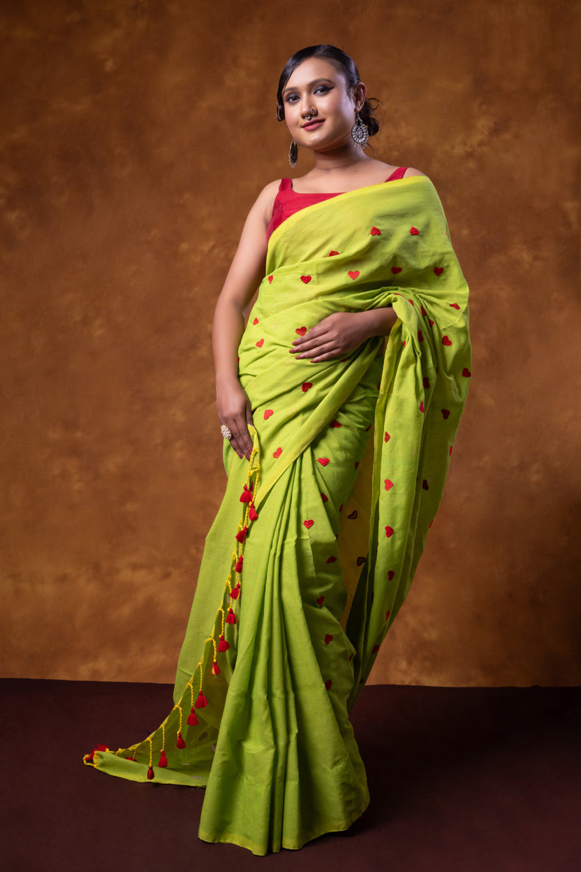 Woman wearing a green saree with red heart patterns against a brown background