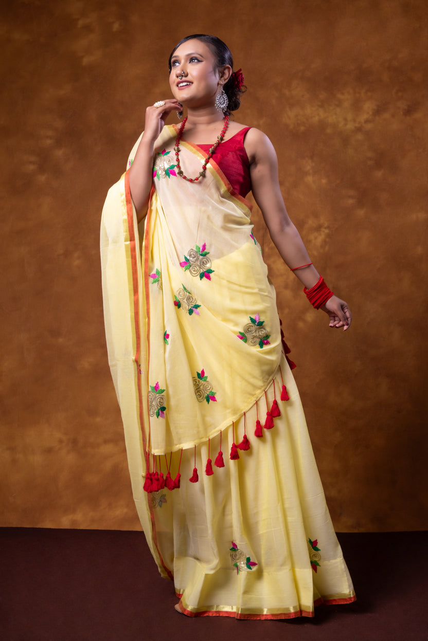 Woman wearing a yellow saree with red accents against a brown background