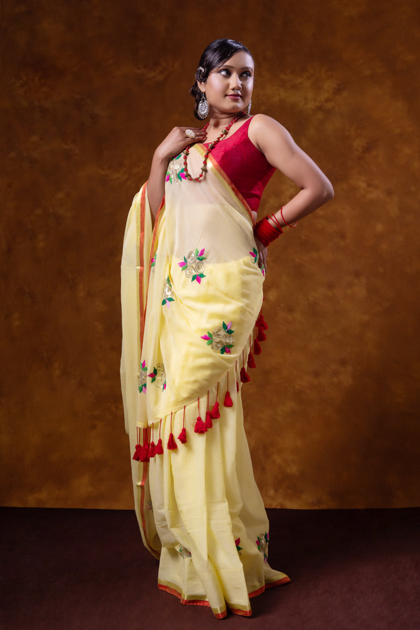 Woman in a yellow saree with red accents against a brown background