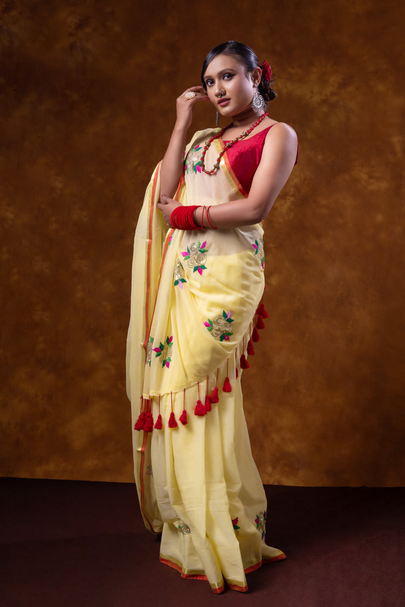 Woman wearing a traditional yellow saree with red accents against a brown background