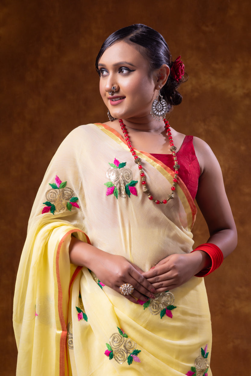 Woman in a traditional yellow saree with red blouse against a brown background