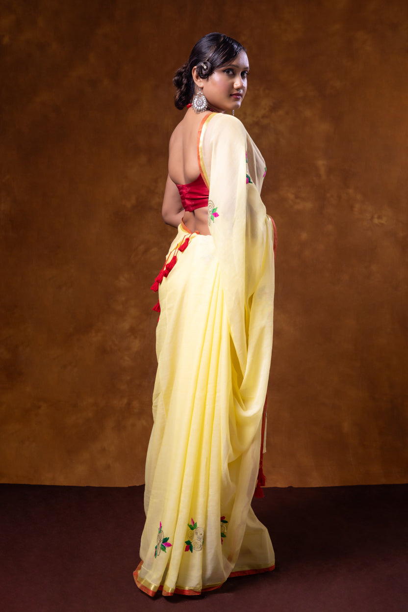 Woman wearing a yellow saree with a red blouse against a brown background