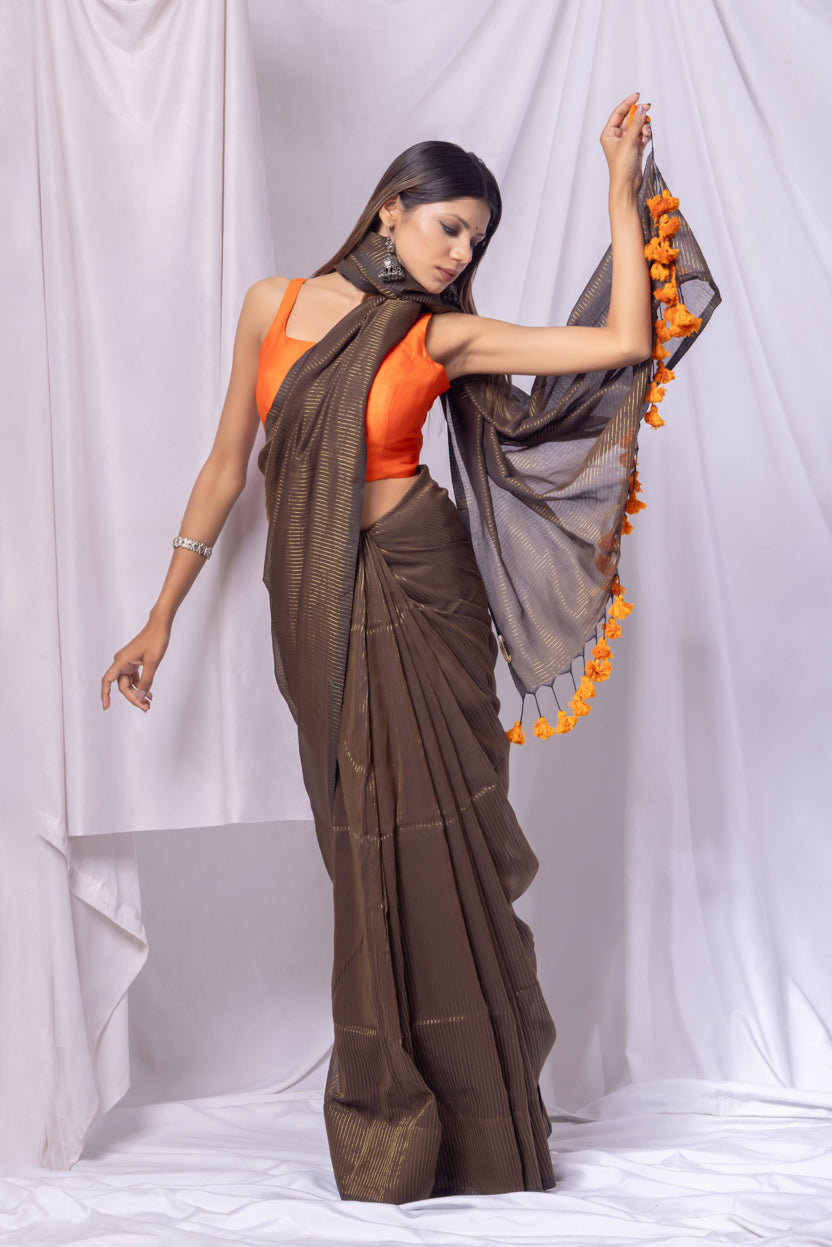 Woman wearing a brown saree with an orange blouse against a white background