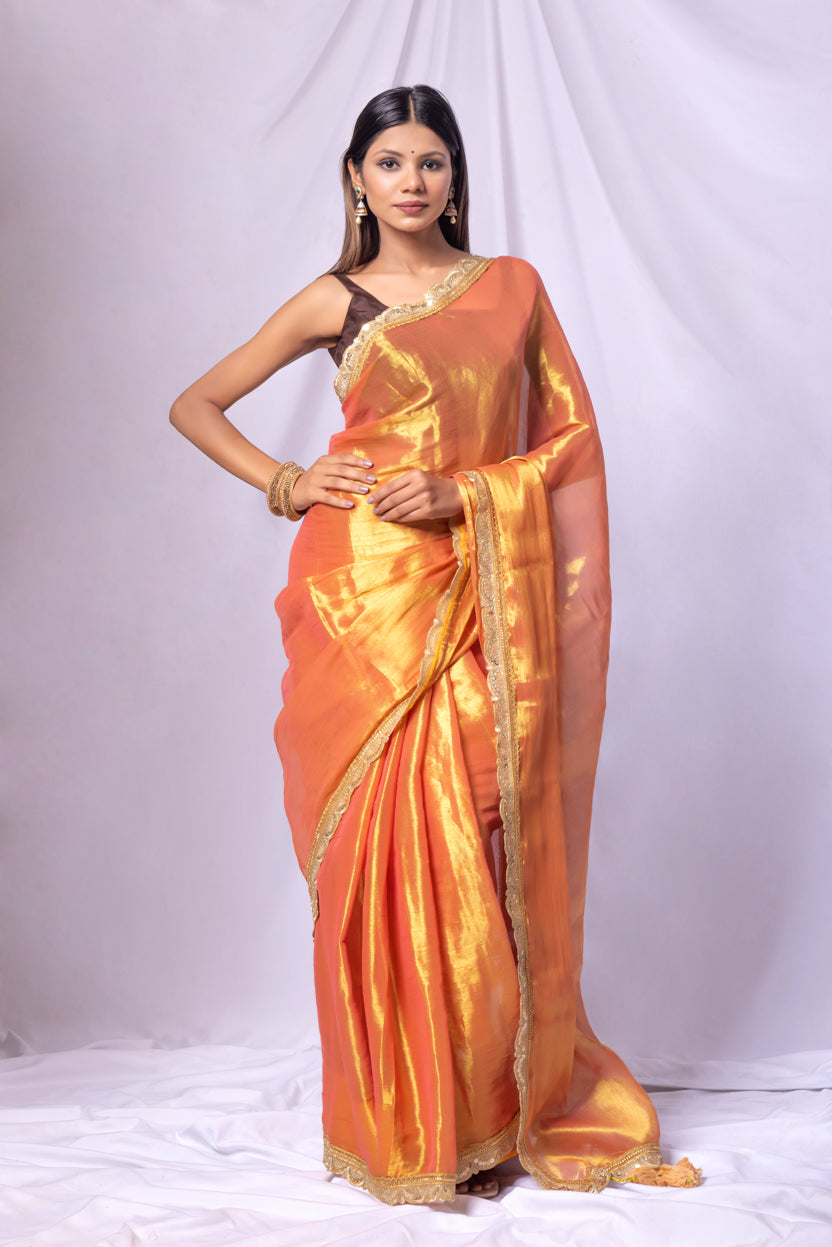 Woman wearing an orange saree with gold border on a white background