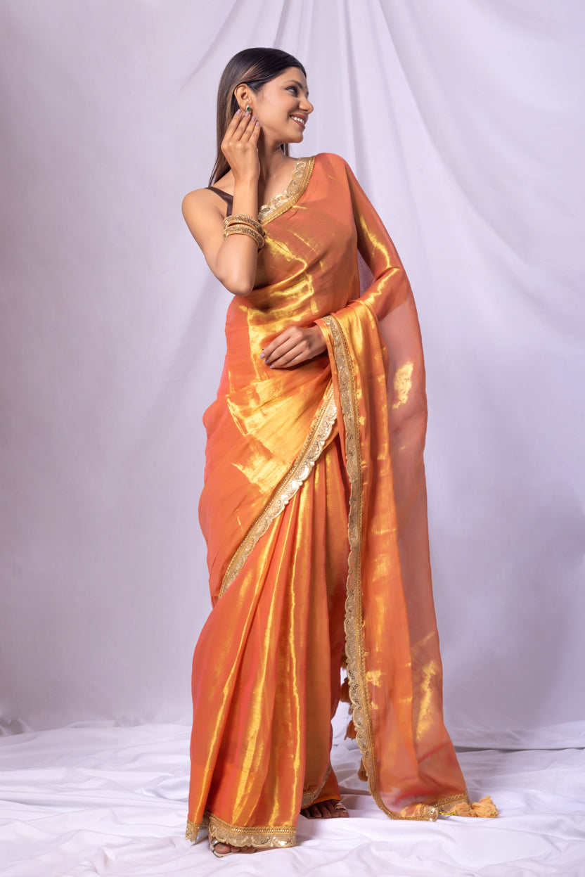 Woman wearing an orange saree with gold border on a white background