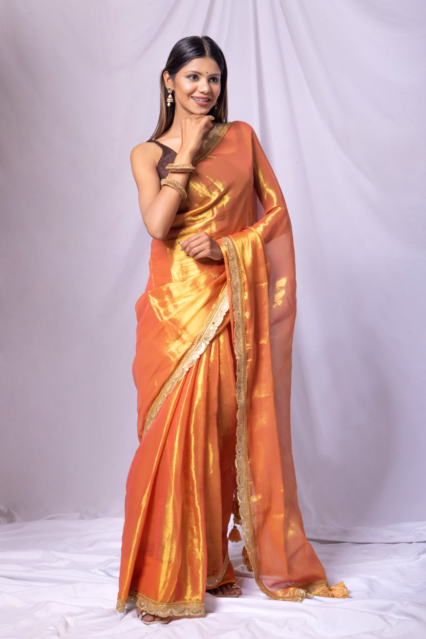 Woman wearing an orange saree with a gold border on a white background