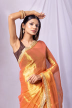 Woman wearing an orange saree with gold border against a white background