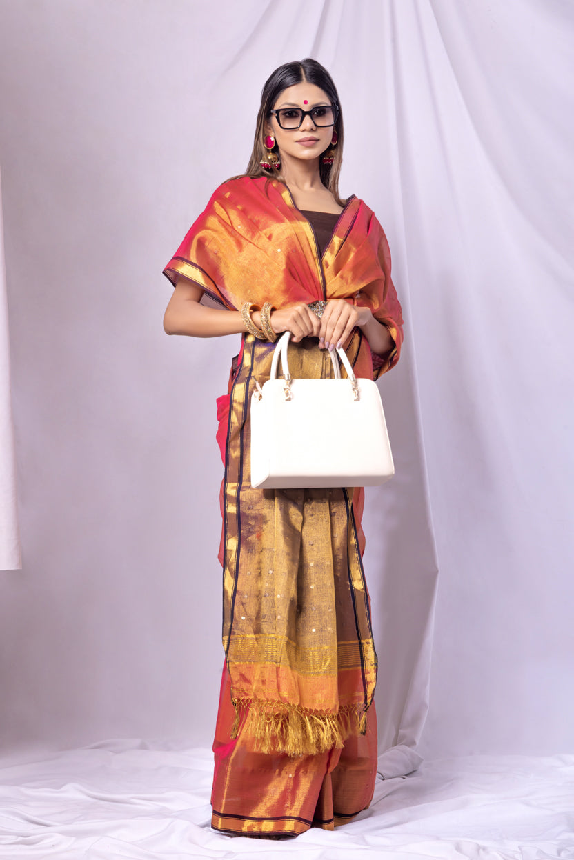 Woman wearing a traditional outfit with a saree and blouse, holding a white handbag on a plain background.