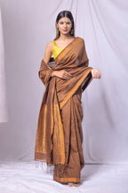 Woman wearing a brown saree with a yellow blouse against a white background