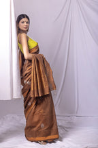 Woman wearing a brown saree with a yellow blouse against a white curtain background
