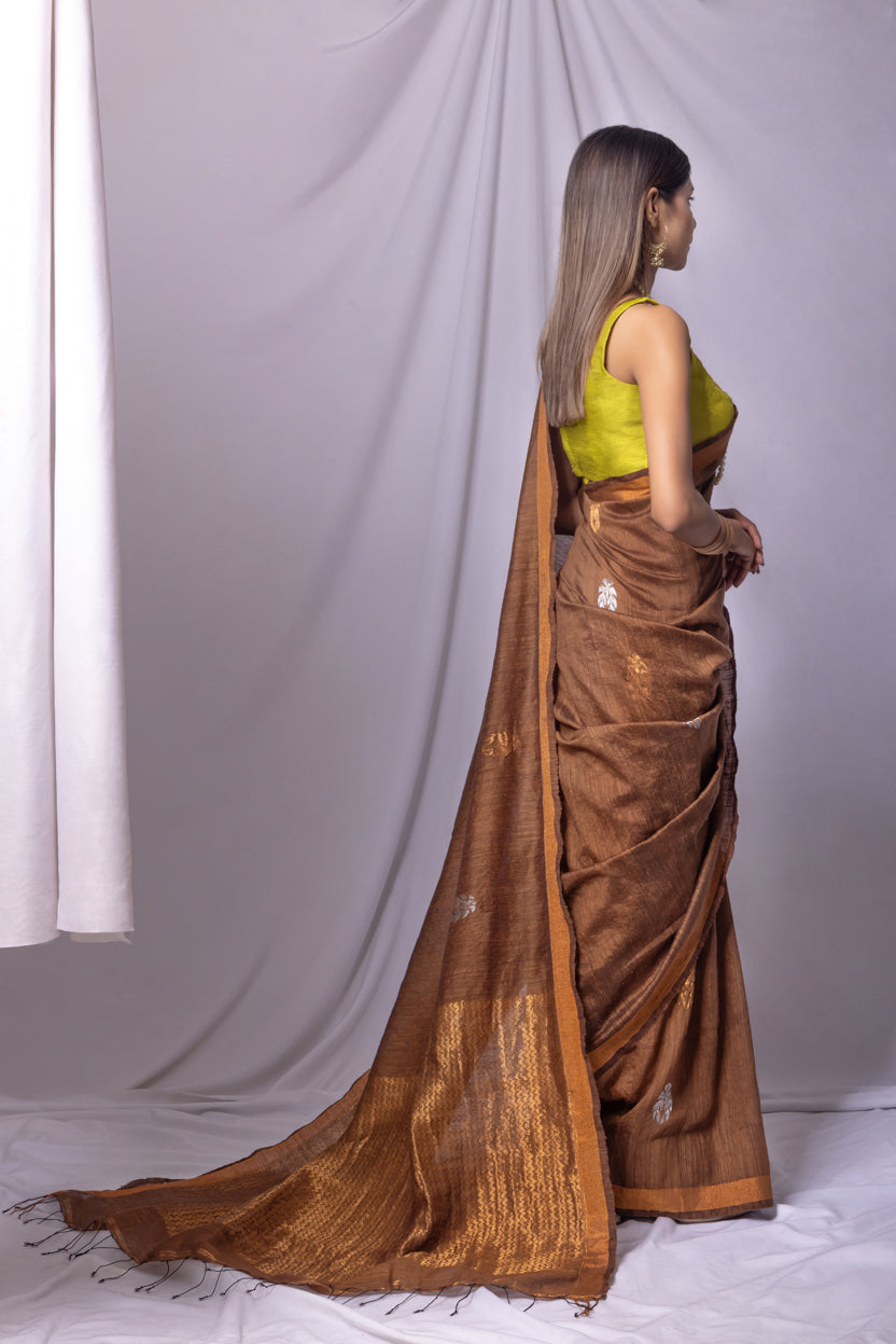 Woman wearing a brown saree with a green blouse against a white curtain background