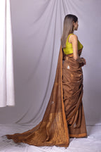 Woman wearing a brown saree with a green blouse against a white curtain background