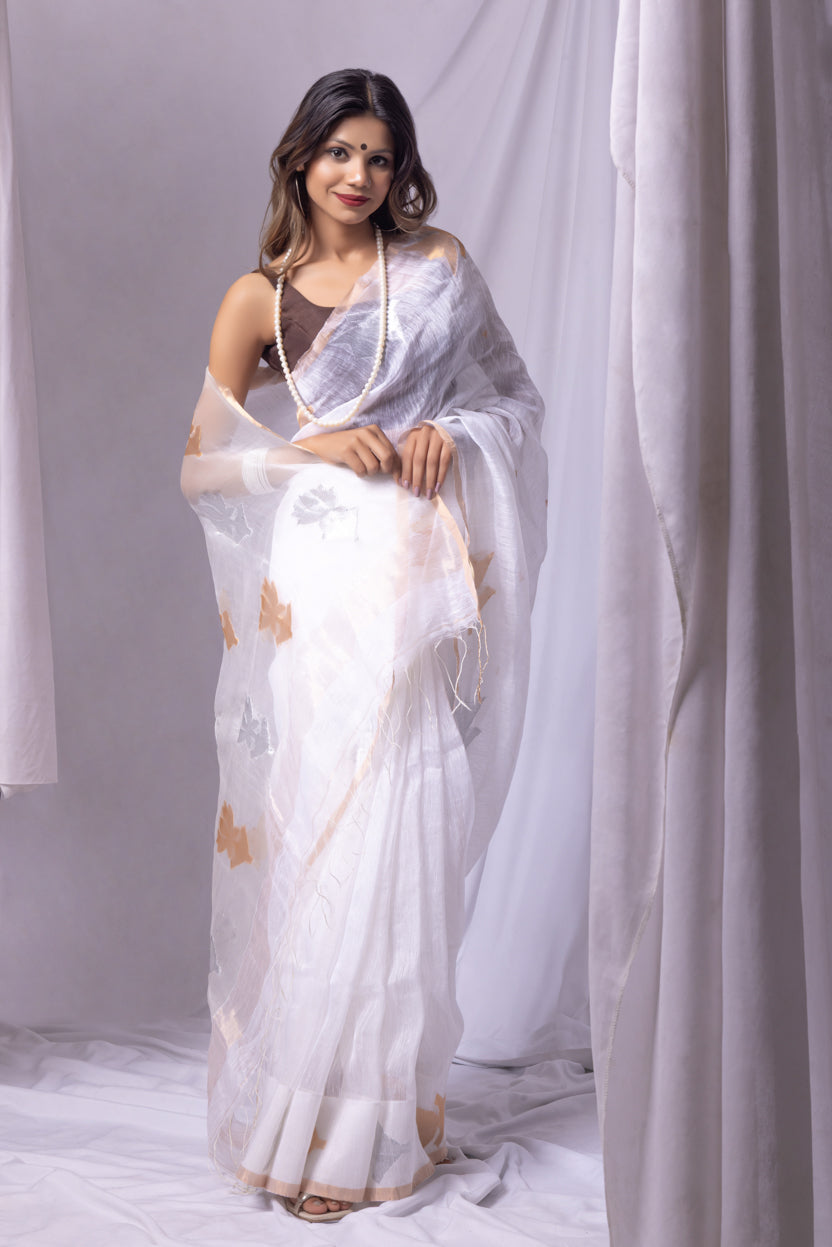 Woman wearing a white saree with gold patterns against a white curtain background
