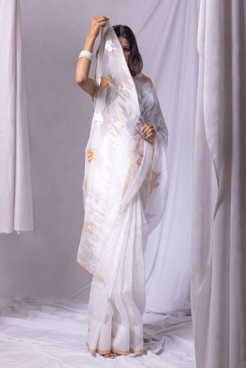 Woman holding a white saree with gold patterns against a plain background