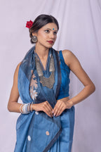 Woman wearing a blue saree with a white blouse against a plain background