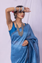 Woman wearing a blue saree with silver jewelry against a white background