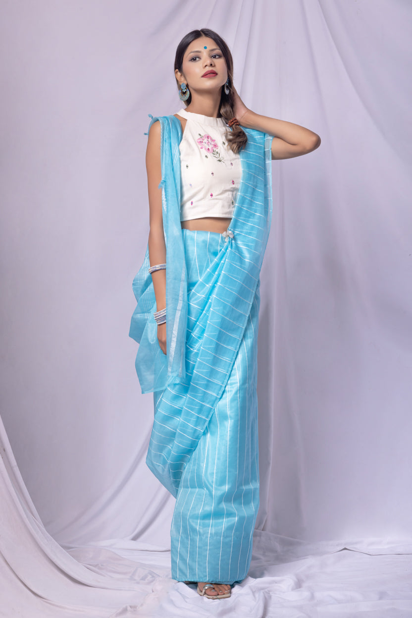 Woman wearing a sky blue saree with a white blouse against a white background