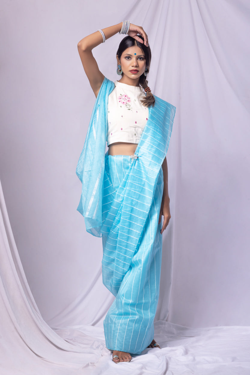 Woman wearing a sky blue saree with a white blouse against a white background