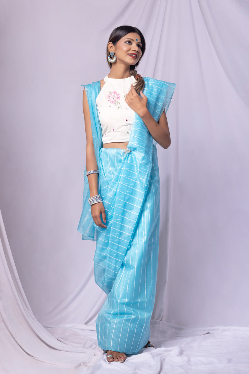 Woman wearing a sky blue saree with a white blouse against a white background