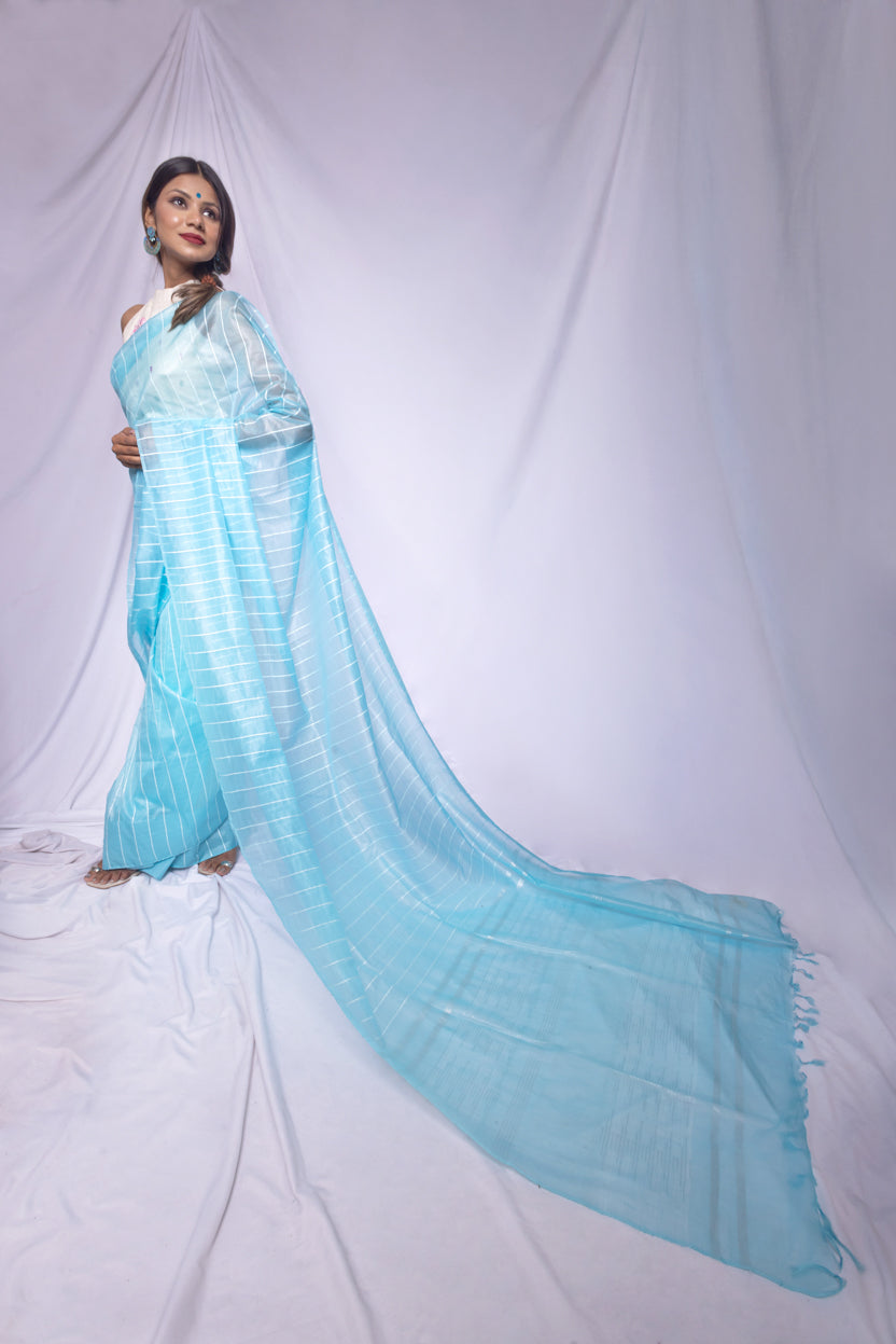 Woman wearing a sky blue saree with a white blouse against a white background