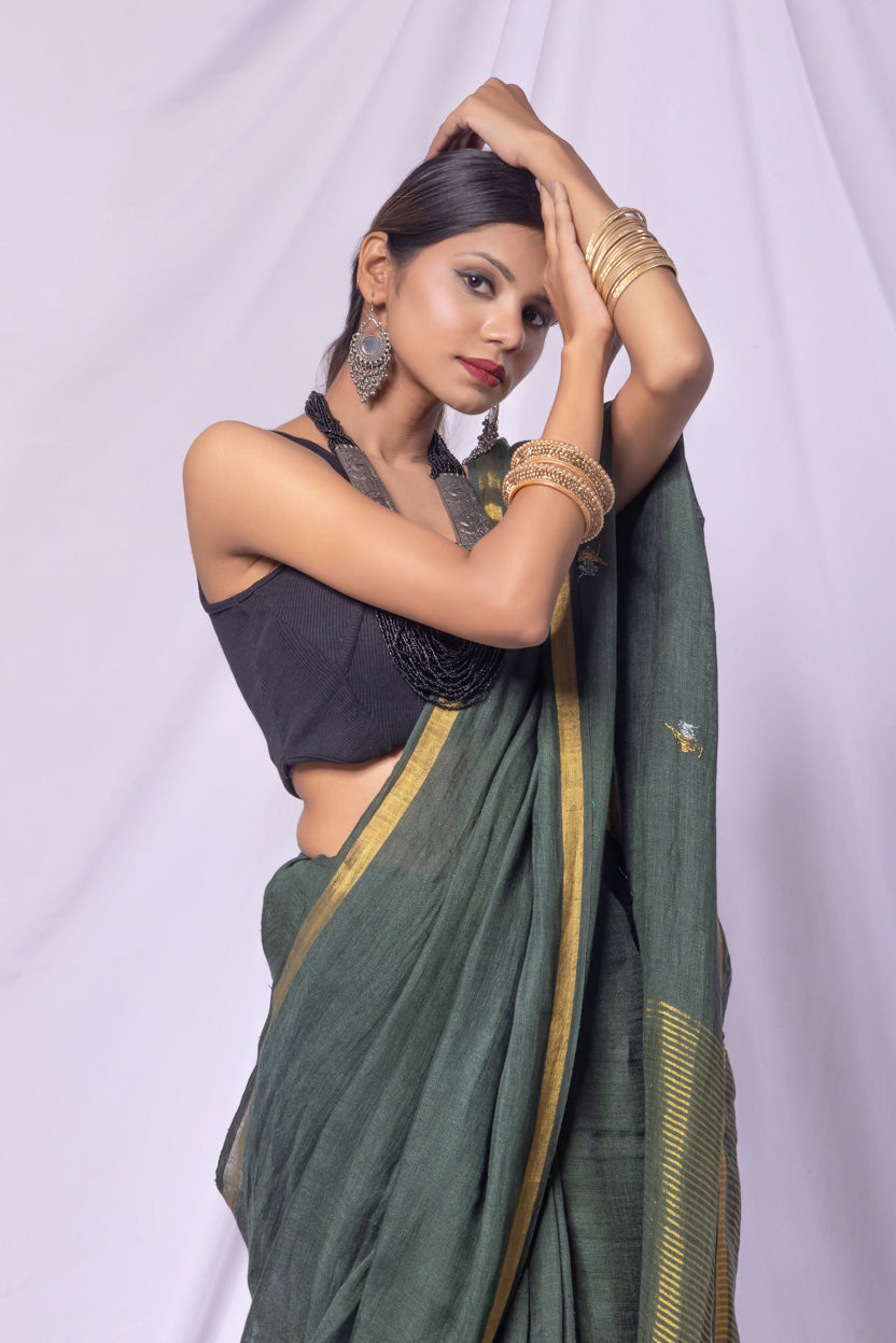 Woman wearing a green saree with a gold border against a white background